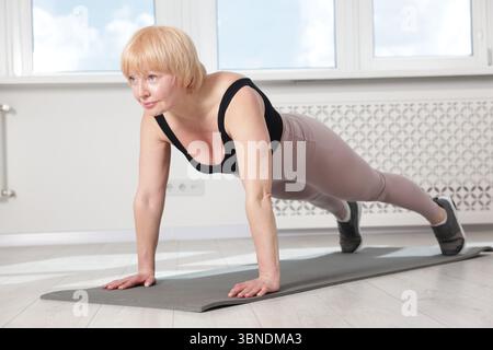 Femme senior dans les vêtements de sport faisant de l'exercice de planche à la maison Banque D'Images