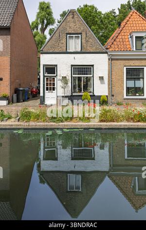 Une charmante maison de canal hollandaise à Delft, magnifiquement reflétée dans l'eau calme, présentant une architecture classique et des fleurs vibrantes au bord du canal. Banque D'Images
