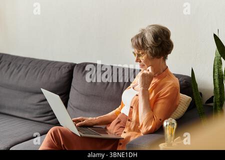 Femme mature se détend à la maison dans une tenue confortable, concentré sur son ordinateur portable dans un environnement confortable. Banque D'Images