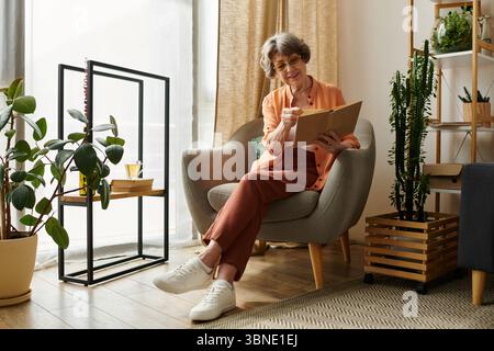 Femme mature habillée confortablement assise dans une chaise confortable, écrivant avec une boisson chaude à proximité. Banque D'Images