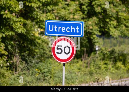 Un panneau d'entrée clair « Utrecht » avec une limite de vitesse de 50 km/h, sur fond de feuillage vert éclatant sous un ciel ensoleillé. Banque D'Images