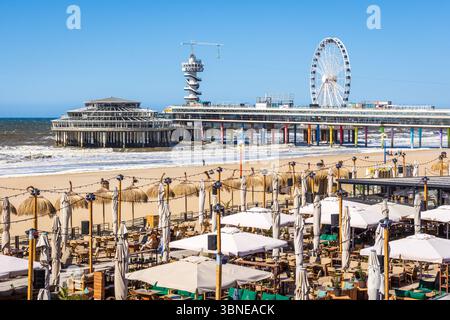 Vue sur la jetée de Scheveningen à la Haye, aux pays-Bas, comprenant une grande roue et une tour de saut à l'élastique, avec des restaurants de plage au premier plan Banque D'Images