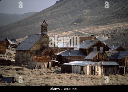 Bodie CA USA 1984. Le département de l'intérieur des États-Unis reconnaît le district historique de Bodie comme un monument historique national. Également enregistrée comme monument historique de Californie, la ville fantôme a été officiellement créée en tant que parc historique d'État de Bodie en 1962. Il reçoit environ 200 000 visiteurs par an. Bodie State Historic Park est en partie soutenu par la Fondation Bodie. En 1876, la Standard Company découvrit un gisement rentable de minerai aurifère, qui transforma Bodie, d'un camp minier isolé comprenant quelques prospecteurs et employés de la compagnie, en une ville-bourgade du Far West. Banque D'Images