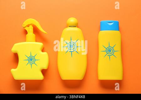 Produits de crème solaire dans des bouteilles avec des dessins de soleil sur fond orange, vue de dessus Banque D'Images