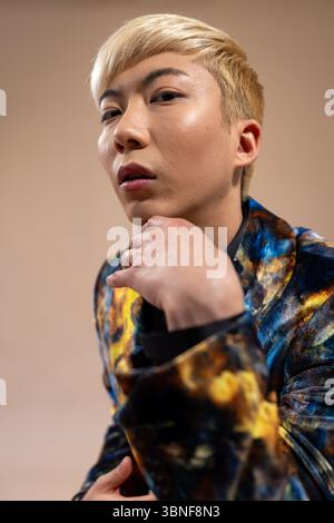 Photo en studio d'un jeune homme adulte posant pour la caméra avec une expression sérieuse. Il a les cheveux décolorés et porte un costume en velours coloré, standi Banque D'Images