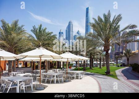 Dubaï, Émirats arabes Unis - 13 mars 2025 : L'espace repas extérieur présente des parasols blancs et des palmiers, avec de superbes gratte-ciel de Dubaï dans le Banque D'Images