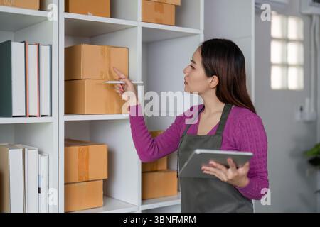 E-commerce et organisation des stocks. Une femme vérifiant les niveaux d'inventaire tout en se préparant pour les ventes en ligne dans un entrepôt bien rangé. Banque D'Images
