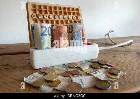 Strompreise Symbolbild Steigender Energiekosten in Deutschland 02.07.25, Eisenbach : Symbolfoto, Illustrationsbild, Symbolbild, Illustrationsfoto, Alltagsszene Symbolbild zum Thema Strompreise : in einer weißen Mehrfachsteckdose stecken zusammengerollte Euro-Geldscheine 20, 10, 50 Euro. Die Steckdose ist eingeschaltet, im Hintergrund steht ein Holzbrett mit Würfeln, die das Wort STROMPREIS bilden. Auf dem Holztisch liegen zusätzlich Münzen und kleinere Geldscheine verteilt. DAS Bild thematisiert die steigenden Kosten für Energie und Strom in Deutschland. Eisenbach Hessen Deutschland *** électrique Banque D'Images