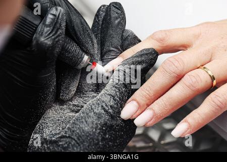 Salon de beauté manucure. Main de femme pendant le soin des ongles. Application de gants noirs et vernis à ongles. Styliste professionnel des ongles. Soin beauté mains propres. Banque D'Images