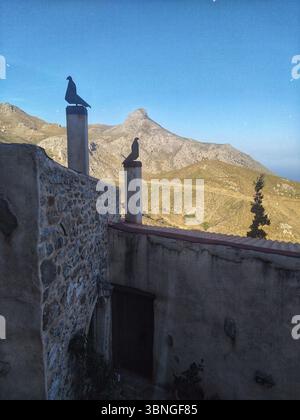 Bâtiment traditionnel en pierre avec des silhouettes artistiques de pigeons sur les cheminées, situé contre un paysage de montagne magnifique dans la Crète rurale, Grèce. Banque D'Images