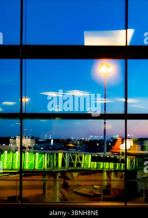 Une fenêtre de terminal de l'aéroport vue au crépuscule, avec un pont à réaction et avion visible au loin. Banque D'Images