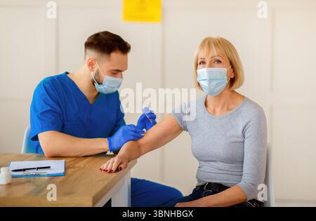Femme caucasienne âgée recevant une injection intramusculaire du vaccin contre le coronavirus pendant rendez-vous du médecin à la clinique Banque D'Images