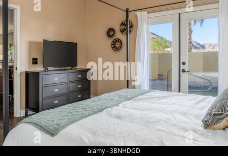 Chambre moderne sur le thème du désert avec lit à baldaquin, commode, télévision à écran plat et portes-fenêtres Banque D'Images