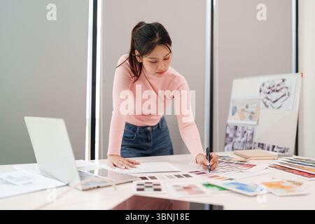Jeune femme asiatique concepteur d'interface utilisateur au travail concevant un site Web et une application mobile. Elle utilise des palettes de couleurs et crée des croquis sur son bureau. Ordinateur portable i Banque D'Images