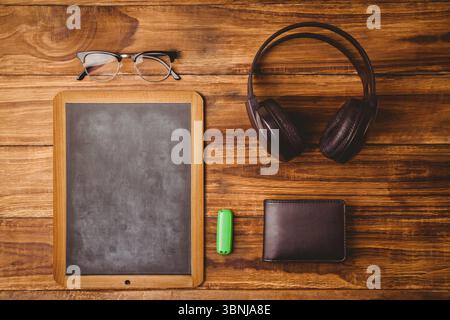 Petit tableau noir est assis sur le bureau en bois dans un design plat, montrant lunettes, écouteurs, portefeuille, USB Banque D'Images