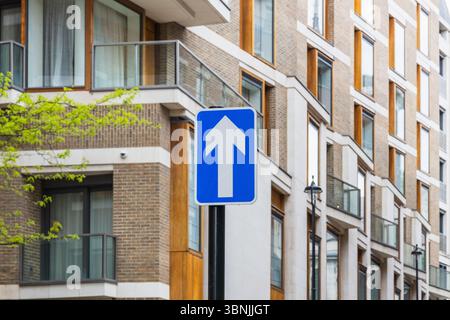 Panneau de signalisation bleu à sens unique avec flèche vers le haut sur la rue moderne de la ville près des appartements contemporains Banque D'Images