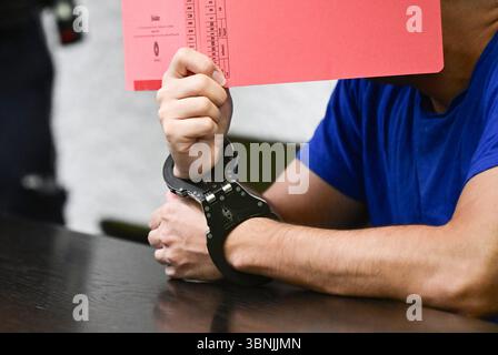Stuttgart, Allemagne. 03 juillet 2025. Un accusé est assis dans la salle d'audience avec des menottes et un dossier devant son visage avant le début de son procès. Un demandeur d'asile iranien aurait assassiné une enseignante de 66 ans à Nürtingen à la mi-octobre 2024 et jeté son corps dans le fleuve Neckar. Crédit : Bernd Weißbrod/dpa/Alamy Live News Banque D'Images