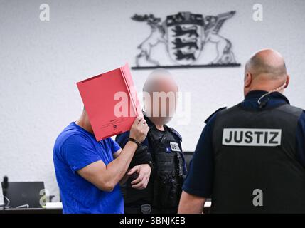 Stuttgart, Allemagne. 03 juillet 2025. Un accusé est conduit dans la salle d'audience avec des menottes et un dossier devant son visage avant le début de son procès. Un demandeur d'asile iranien aurait assassiné une enseignante de 66 ans à Nürtingen à la mi-octobre 2024 et jeté son corps dans le fleuve Neckar. Crédit : Bernd Weißbrod/dpa/Alamy Live News Banque D'Images