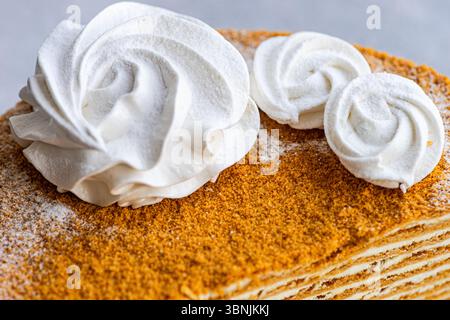 Gros plan d'un gâteau au miel fait maison, parfaitement complété par une sauce à la crème sure soyeuse et élégamment décoré avec des guimauves zephyr à la vanille. Banque D'Images