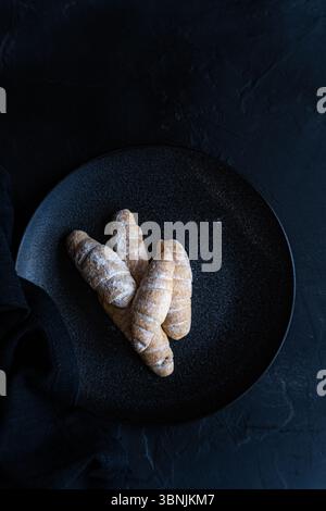 D’en haut, une sélection de pâtisseries maison est disposée sur une assiette en céramique foncée, mettant en valeur leurs croûtes brunes dorées et un saupoudrage de sucre en poudre Banque D'Images