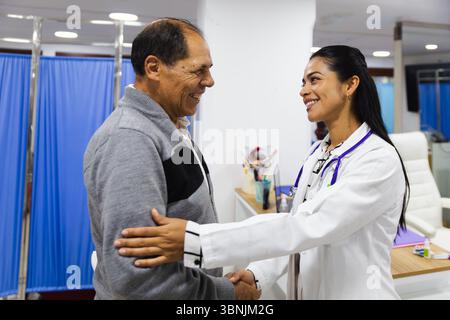 Une jeune femme médecin souriante fournit des soins attentifs à un patient âgé masculin dans un hôpital latino-américain, favorisant la confiance et des soins de santé positifs Banque D'Images