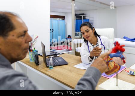 Une jeune femme médecin fournit des soins professionnels à un patient âgé de sexe masculin dans un hôpital latino-américain. Elle explique attentivement les informations médicales, Banque D'Images