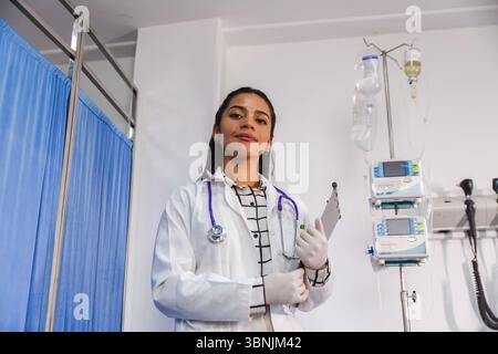 Une femme médecin confiante se tient dans un cadre hospitalier, tenant une planche à pince et portant un manteau blanc et un stéthoscope, signifiant professionnalisme et h. Banque D'Images