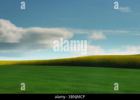 Vaste paysage avec des collines verdoyantes sous un ciel bleu clair avec des nuages blancs moelleux. Une bande de coupe jaune ajoute un contraste éclatant à t Banque D'Images