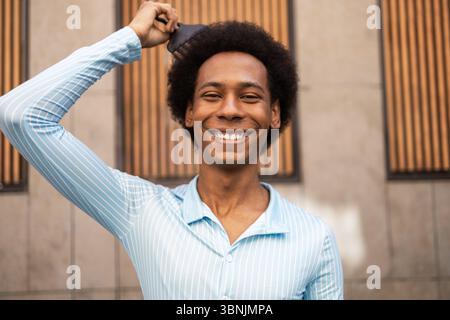 Un individu joyeux non binaire avec une coiffure afro poutres sur un fond urbain. La personne, d'ethnicité mixte, embrasse son identité tout en Banque D'Images