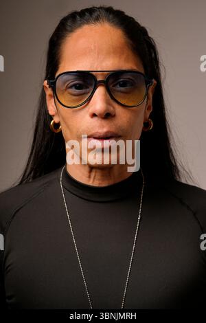 Portrait en gros plan d'un homme latin portant des lunettes surdimensionnées et une chemise noire. Son regard confiant et expressif est parfait pour représenter l'individualité Banque D'Images