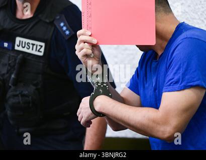 Stuttgart, Allemagne. 03 juillet 2025. Un accusé est conduit dans la salle d'audience avec des menottes et un dossier devant son visage avant le début de son procès. Un demandeur d'asile iranien aurait assassiné une enseignante de 66 ans à Nürtingen à la mi-octobre 2024 et jeté son corps dans le fleuve Neckar. Crédit : Bernd Weißbrod/dpa/Alamy Live News Banque D'Images