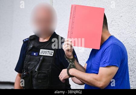 Stuttgart, Allemagne. 03 juillet 2025. Un accusé est conduit dans la salle d'audience avec des menottes et un dossier devant son visage avant le début de son procès. Un demandeur d'asile iranien aurait assassiné une enseignante de 66 ans à Nürtingen à la mi-octobre 2024 et jeté son corps dans le fleuve Neckar. Crédit : Bernd Weißbrod/dpa - ATTENTION : officiel a été pixélisé pour des raisons légales/dpa/Alamy Live News Banque D'Images