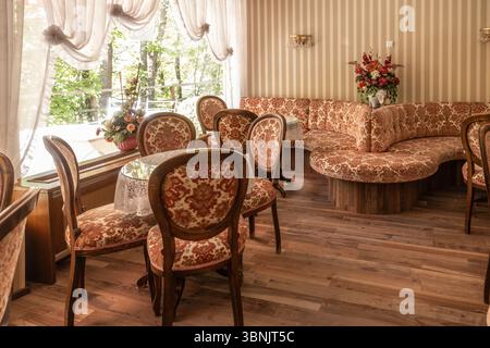 Un charmant intérieur de café rétro avec un décor vintage, une élégante sellerie florale, des meubles en bois et une lumière naturelle douce à travers de grandes fenêtres, cre Banque D'Images