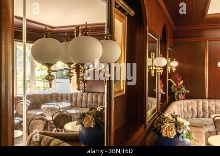 Un intérieur de café rétro confortable avec des sièges touffetés et des luminaires en laiton, évoquant une atmosphère vintage avec d'élégants boiseries et des motifs floraux Banque D'Images