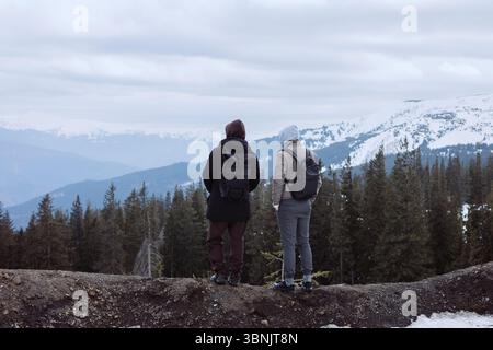 Deux randonneurs se tiennent sur un sentier enneigé, entouré de majestueuses vues sur les montagnes et de pins. Le paysage hivernal offre une atmosphère sereine pour explorer Banque D'Images