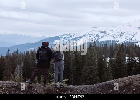 Deux randonneurs se tiennent sur un sentier enneigé, entouré de majestueuses vues sur les montagnes et de pins. Le paysage hivernal offre une atmosphère sereine pour explorer Banque D'Images