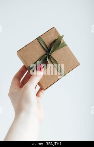 Une femme tient une petite boîte cadeau élégamment emballée avec un ruban vert, créant un sentiment d'anticipation et de célébration. La simplicité et l'élégance o Banque D'Images