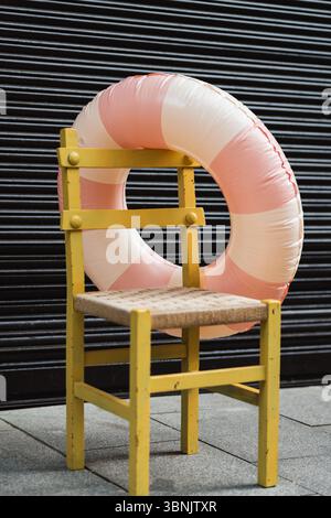 Une scène estivale vibrante avec une chaise en bois jaune vintage jumelée à un anneau gonflable rose et blanc, sur un fond sombre et élégant, capt Banque D'Images