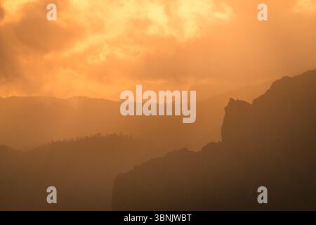 Vue panoramique d'un coucher de soleil à Gran Canaria, Espagne, avec des montagnes silhouettées sur un ciel doré vibrant. Les nuages créent un atmos dramatique et serein Banque D'Images