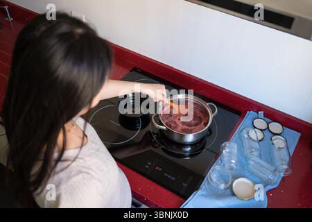 Jeune femme asiatique faisant habilement de la confiture de fraises maison dans une cuisine confortable. Mettant l'accent sur la cuisine artisanale, durable et un style de vie zéro déchet Banque D'Images
