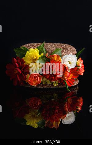 Un sandwich unique habilement arrangé avec des fleurs rouges, jaunes et blanches vives entre deux tranches de pain noir. Les fleurs créent un contraste époustouflant Banque D'Images