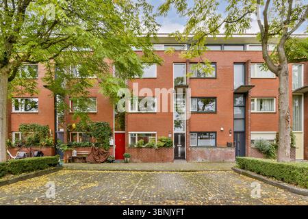 Un bâtiment résidentiel contemporain à l'architecture en briques rouges, encadré par des arbres luxuriants et des feuillages d'automne, créant une atmosphère urbaine accueillante Banque D'Images