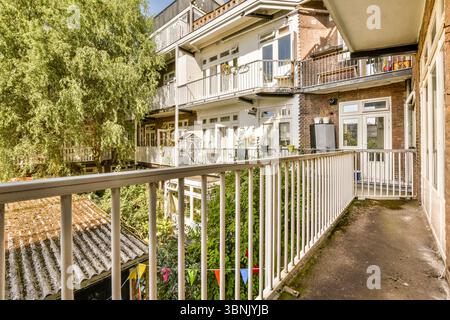Vue sur le balcon surplombant le jardin luxuriant et les appartements voisins, mettant en valeur un paysage extérieur serein et une verdure vibrante sous le soleil. Banque D'Images
