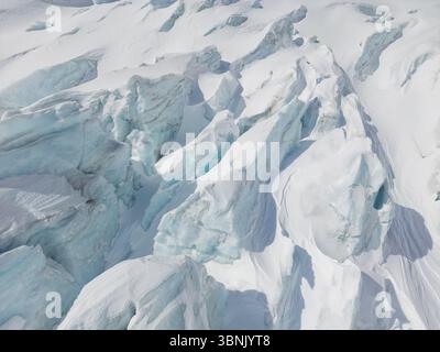 Vue aérienne époustouflante d'un vaste glacier des Alpes suisses présentant d'imposantes formations glaciaires et de profondes crevasses, soulignant la beauté et la fragilité de ce glacier Banque D'Images