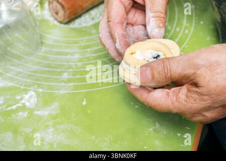 Mains fabriquant des petits pains faits maison avec une garniture crémeuse de fromage cottage, prêts à la cuisson. L'ambiance rustique de la cuisine renforce l'attrait de ces deliciou Banque D'Images