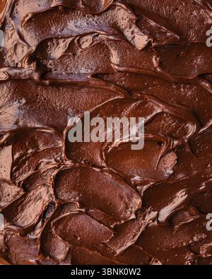 Un gros plan de glaçage au chocolat riche et crémeux étalé en douceur sur une délicieuse surface de gâteau, mettant en valeur sa texture brillante et son apparan invitant Banque D'Images