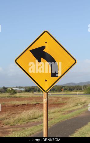 Panneau routier jaune Left Curve monté sur un poteau métallique dans un environnement rural Banque D'Images