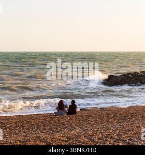 Couple de personnes Sat sur Shingle Beach à Rottingdean en début de soirée lumière regardant vers la Manche Banque D'Images