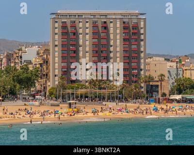 Un grand immeuble résidentiel avec balcons rouges distinctifs donnant sur la plage animée de Barcelone. Banque D'Images