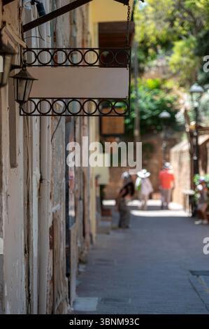 Panneau blanc accroché sur un mur à côté d'une rue étroite avec des piétons explorant à proximité. Banque D'Images